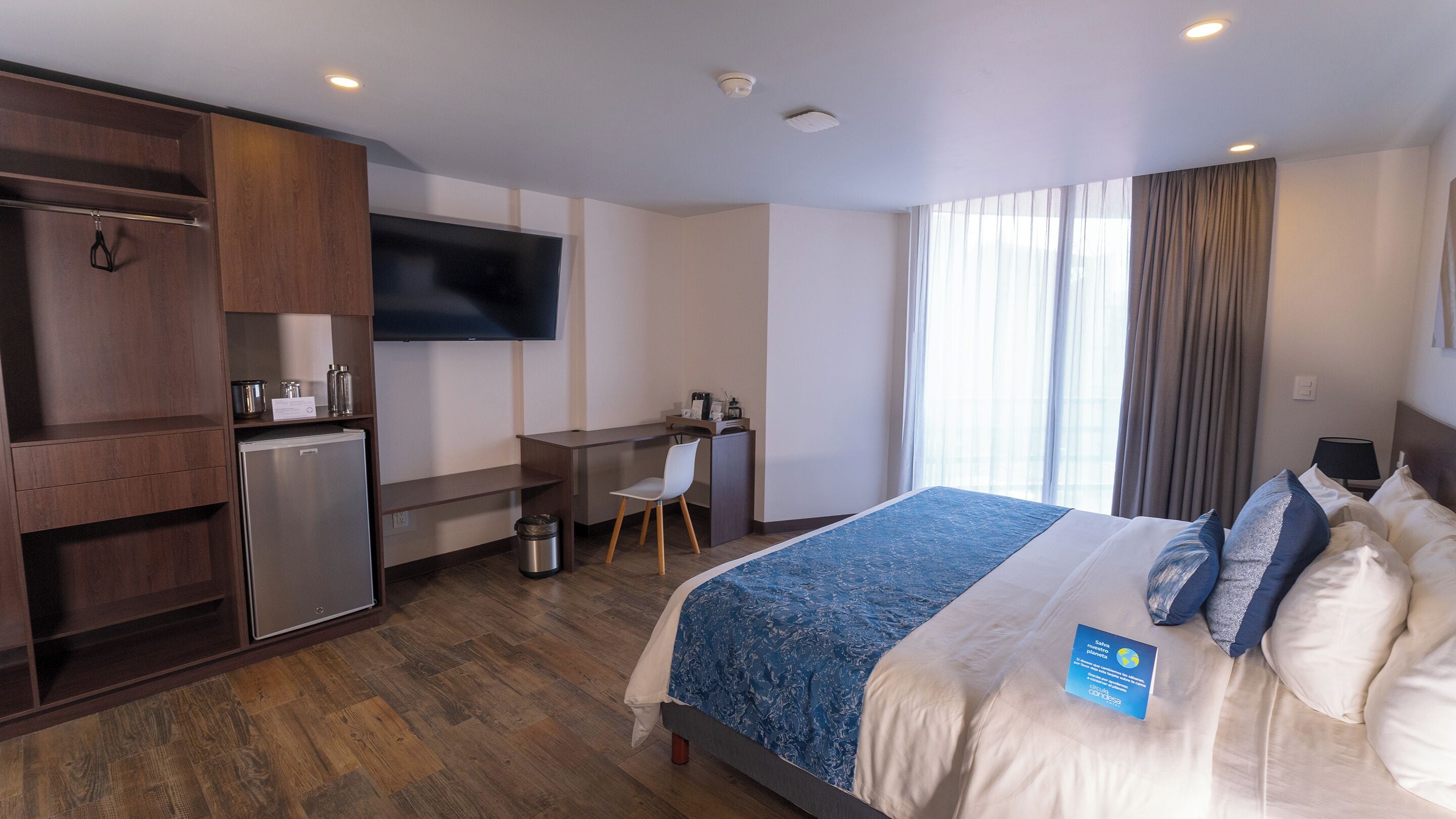 Una habitación de hotel con cama, escritorio, televisión y minibar.
