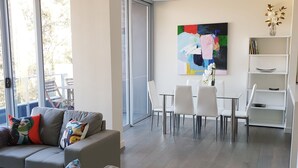 A modern living room with a grey sofa, a dining area with white chairs, and a large abstract painting on the wall. - Modern 2b2b apartmemt. close to water front (Point Frederick)