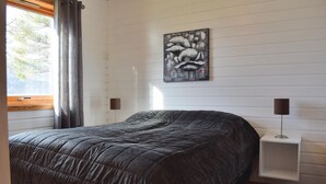 Un dormitorio con una cama grande, una ventana con cortinas, una obra de arte en la pared y una mesita de noche con una lámpara.
