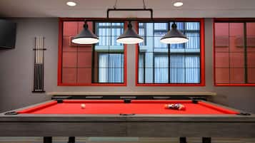 A pool table with three overhead lamps, a red pool table cloth, and a billiard cue.