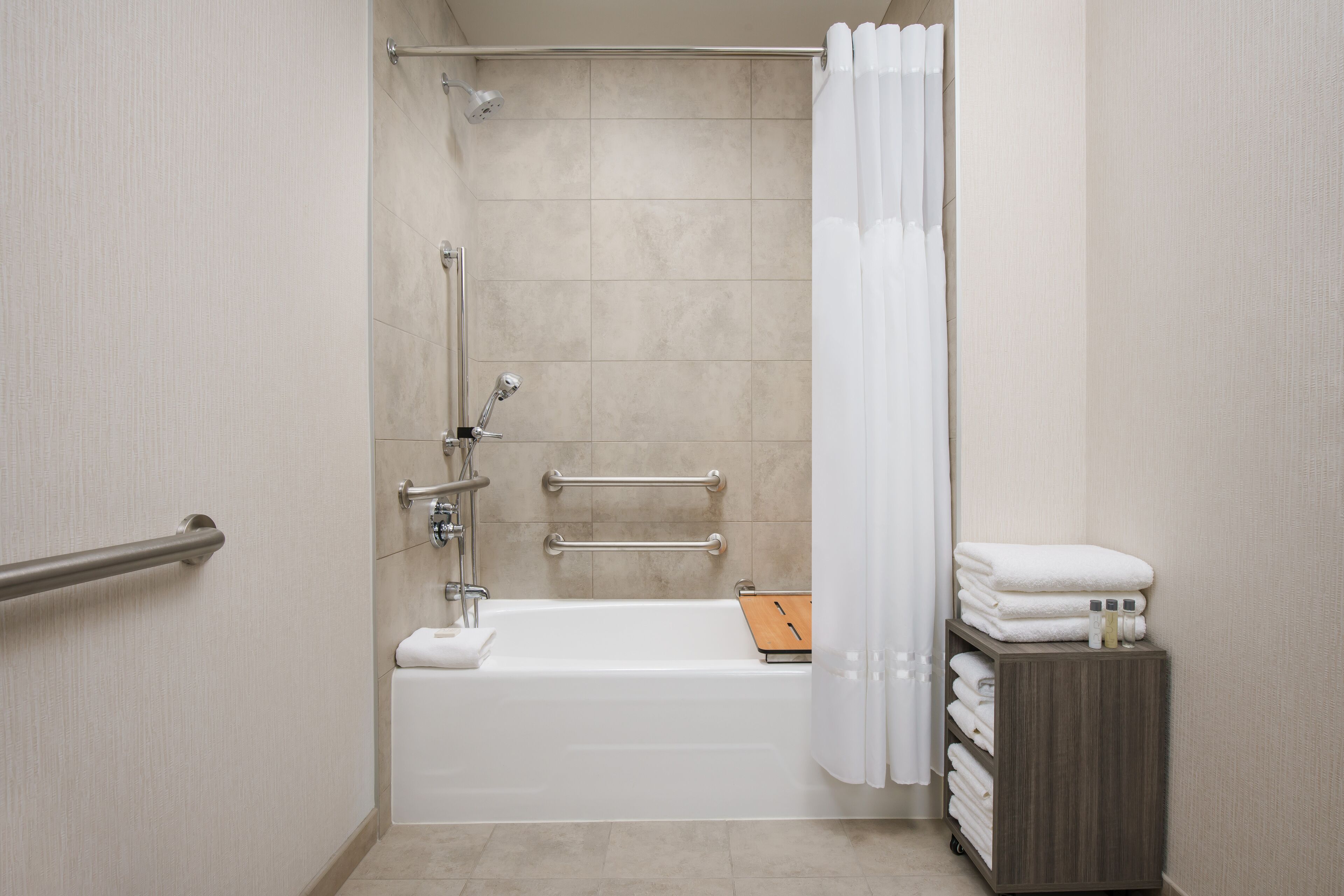 A modern bathroom with a bathtub, grab bars, a showerhead, and a towel rack.