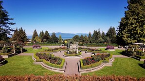 A landscaped garden with a central fountain, surrounded by manicured lawns and flower beds, with a view of mountains in the distance.