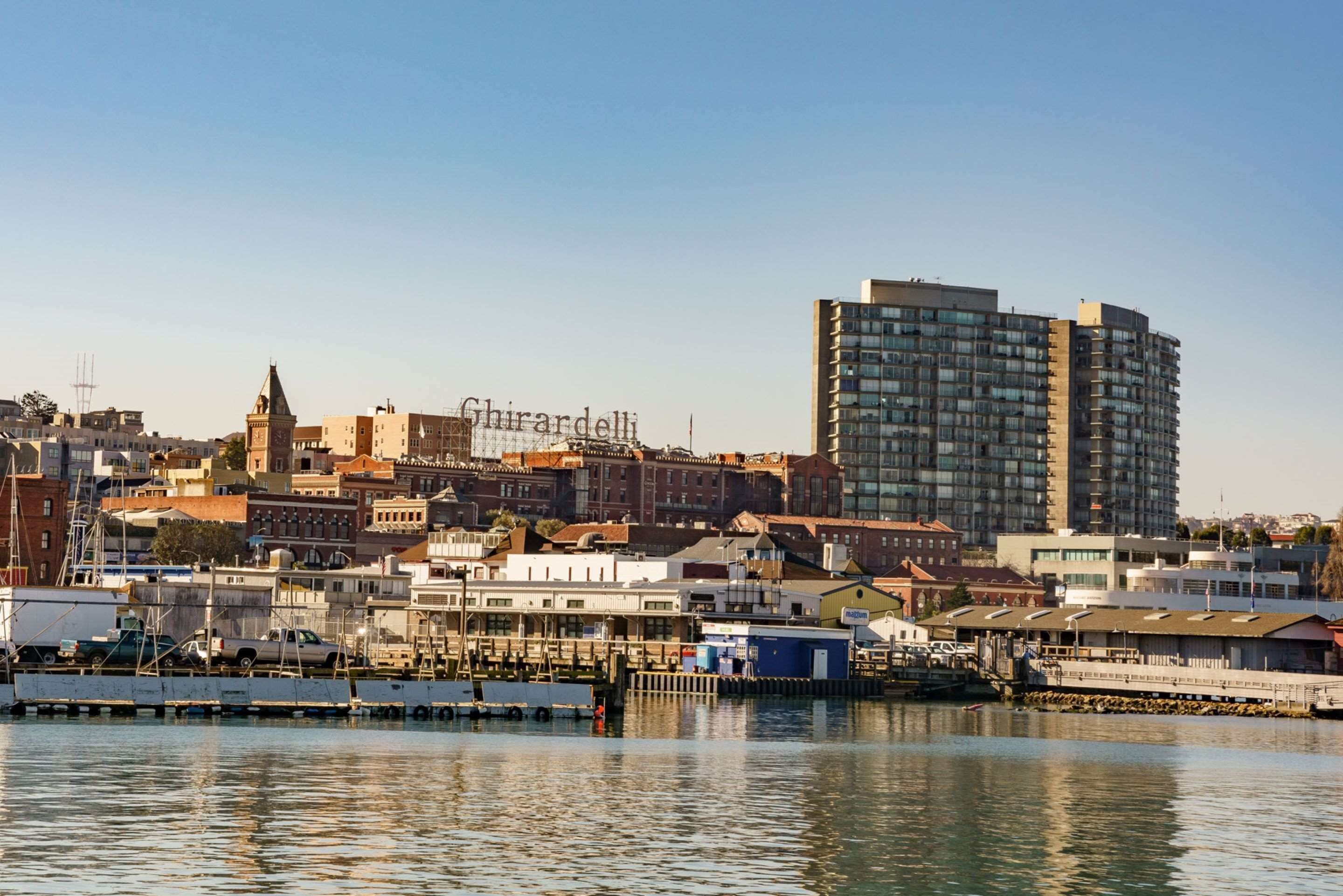 A waterfront cityscape with a prominent high-rise building, a historic church, and a marina with boats.