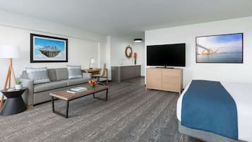 A modern hotel room with a sofa, a coffee table, a TV, a bed, and a small kitchenette.