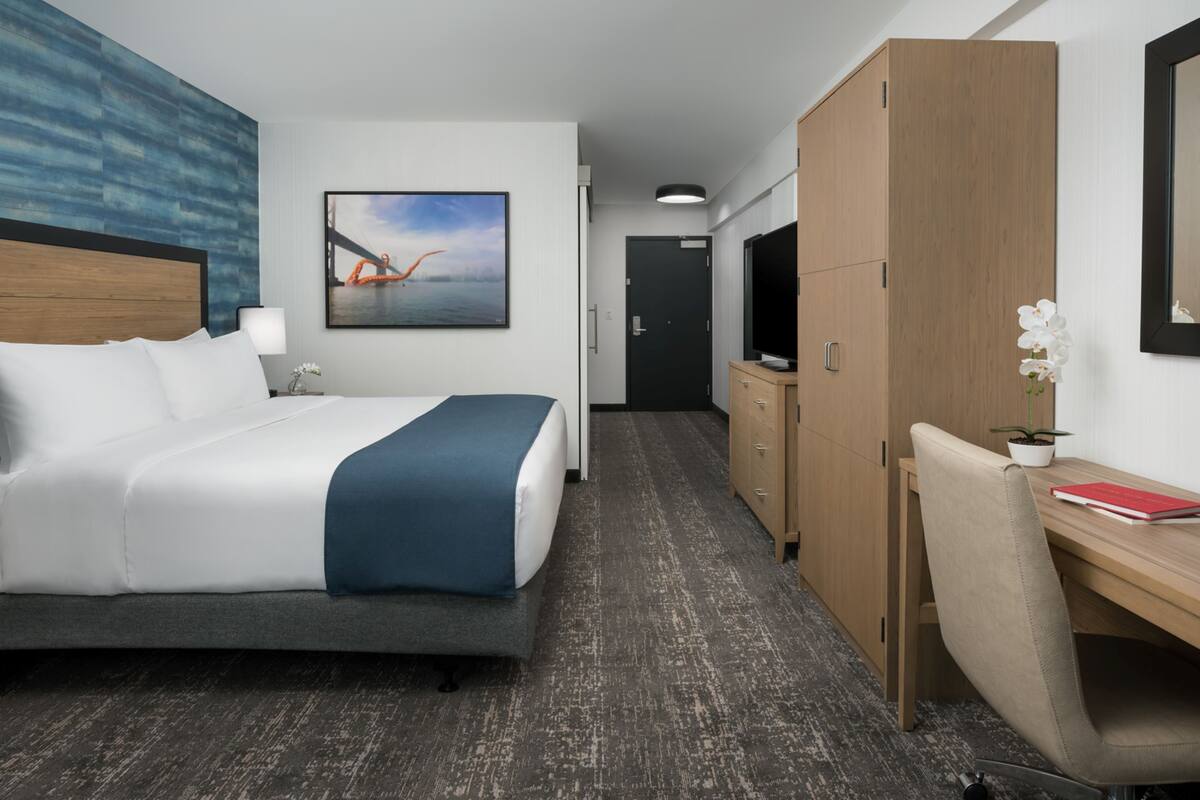 Camera d'albergo con letto, scrivania, televisione, armadio e un quadro appeso al muro.