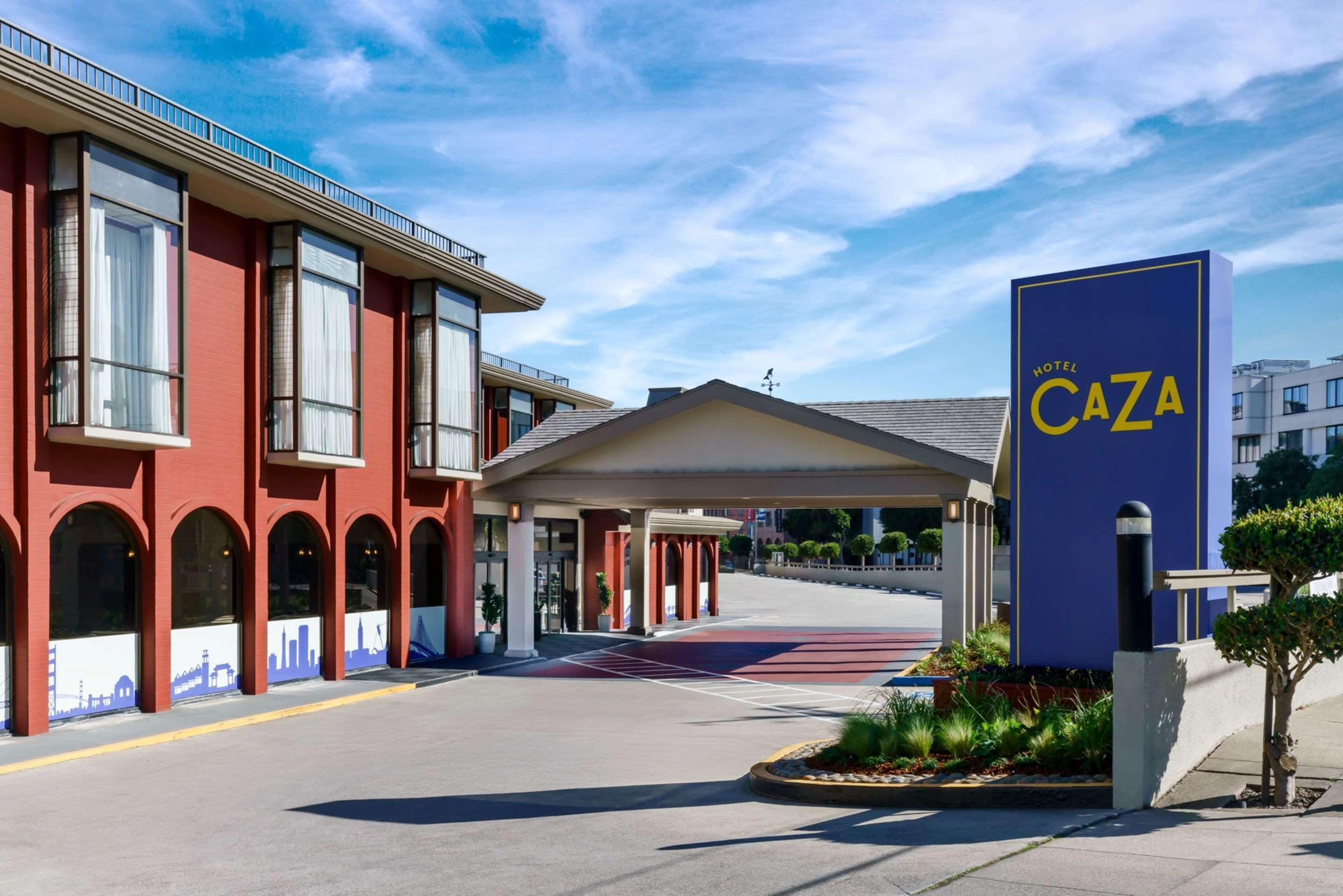 A hotel entrance with a red facade, a blue sign reading "Hotel Caza," and a covered walkway leading to the entrance.
