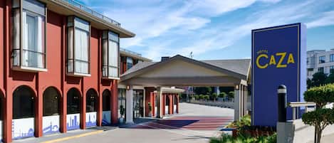A hotel entrance with a red facade, a blue sign reading "Hotel Caza," and a covered walkway leading to the entrance.