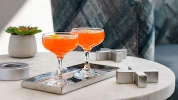 Two martini glasses with orange cocktails on a tray, a small potted plant, and geometric metal blocks on a round table.