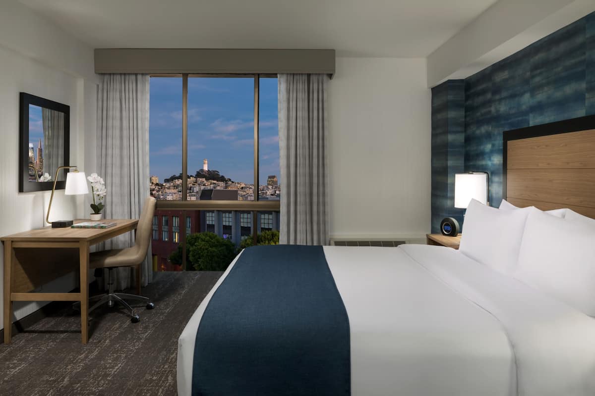 Camera d'albergo con un letto grande, una scrivania e una sedia. Si vede una finestra con vista sulla città.