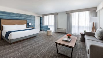 A hotel room with a bed, a sofa, a coffee table, a chair, and a window with curtains.