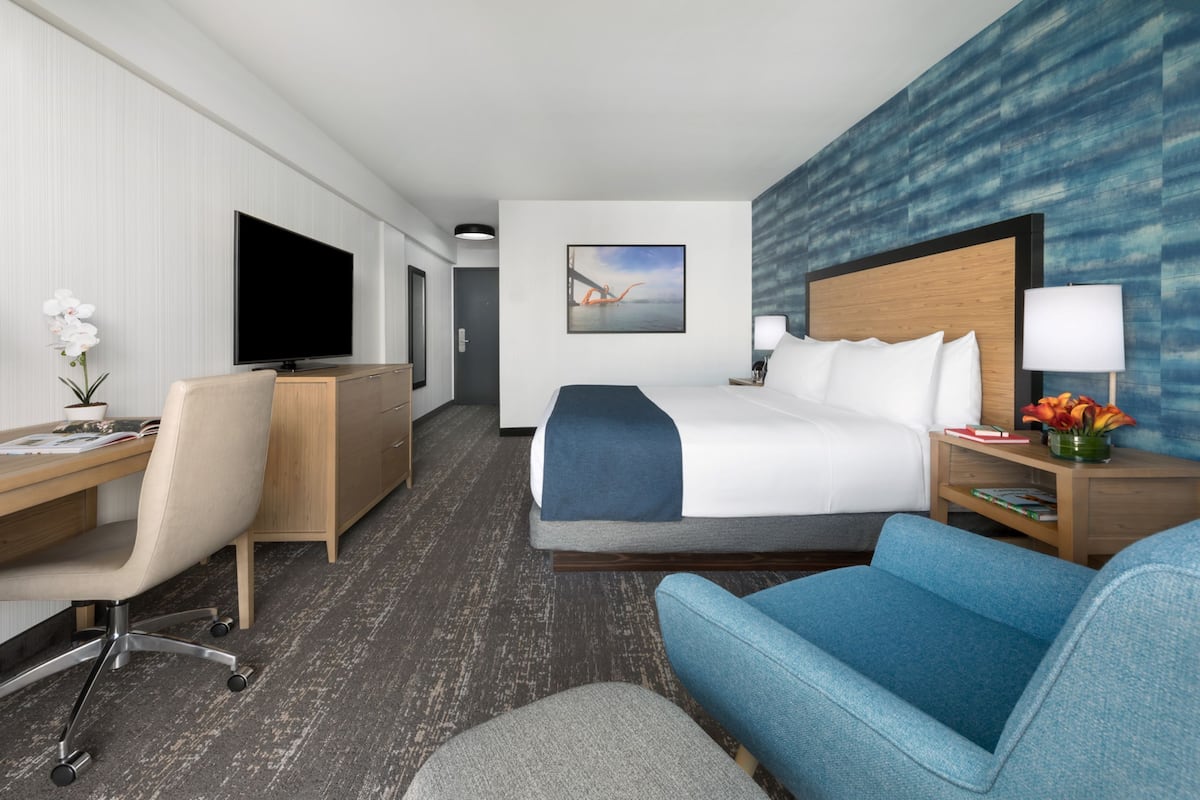 Una camera d'albergo con un letto, una scrivania, una sedia, una televisione e un quadro appeso al muro.