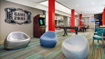 Un espace de jeux avec des fauteuils en forme de sac de haricots, une table de billard et un panneau indiquant « ZONE DE JEUX ».