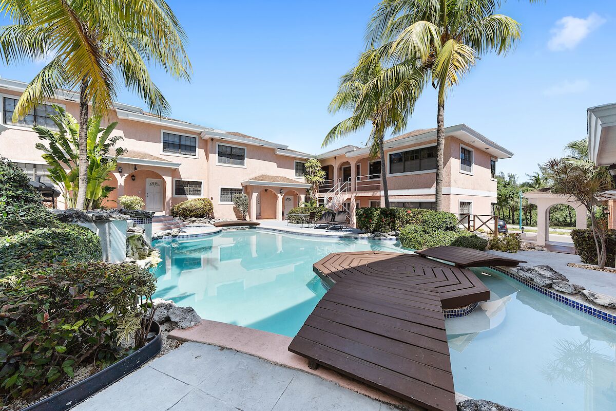 A pool area with a wooden deck, palm trees, and a building with multiple windows and balconies.