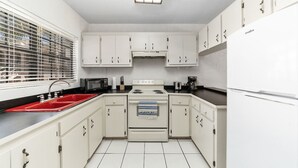 Een kleine keuken met witte kastjes, een rode gootsteen, een fornuis en een koelkast.