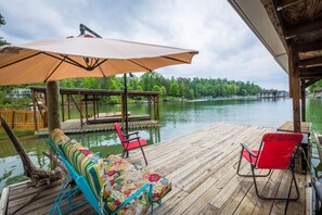 A wooden deck with a covered seating area, a view of a lake, and a dock extending into the water. - PRIVATE LAKEFRONT HOME (Morganton)