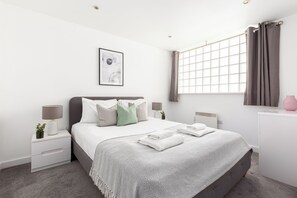 A modern bedroom with a bed, bedside tables, a window with curtains, and a wall-mounted picture. - 2 Bed Flat off Brick Lane (London)
