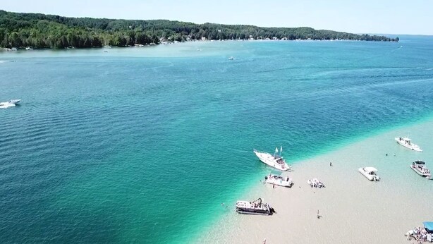 A coastal area with boats anchored near the shore, a sandy beach, and a forested coastline. - Come and enjoy beautiful Torch Lake! (Bellaire)