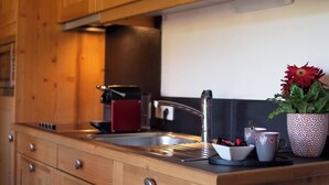 Una cocina con armarios de madera, un lavamanos de acero inoxidable y una tetera roja.