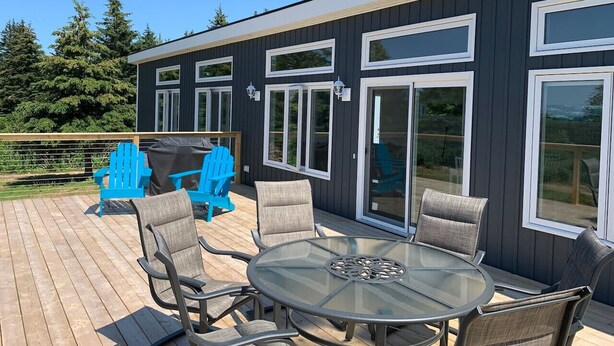 Een terras met een tafel en stoelen met een glazen blad, een barbecue en een blauwe Adirondack-stoel.
