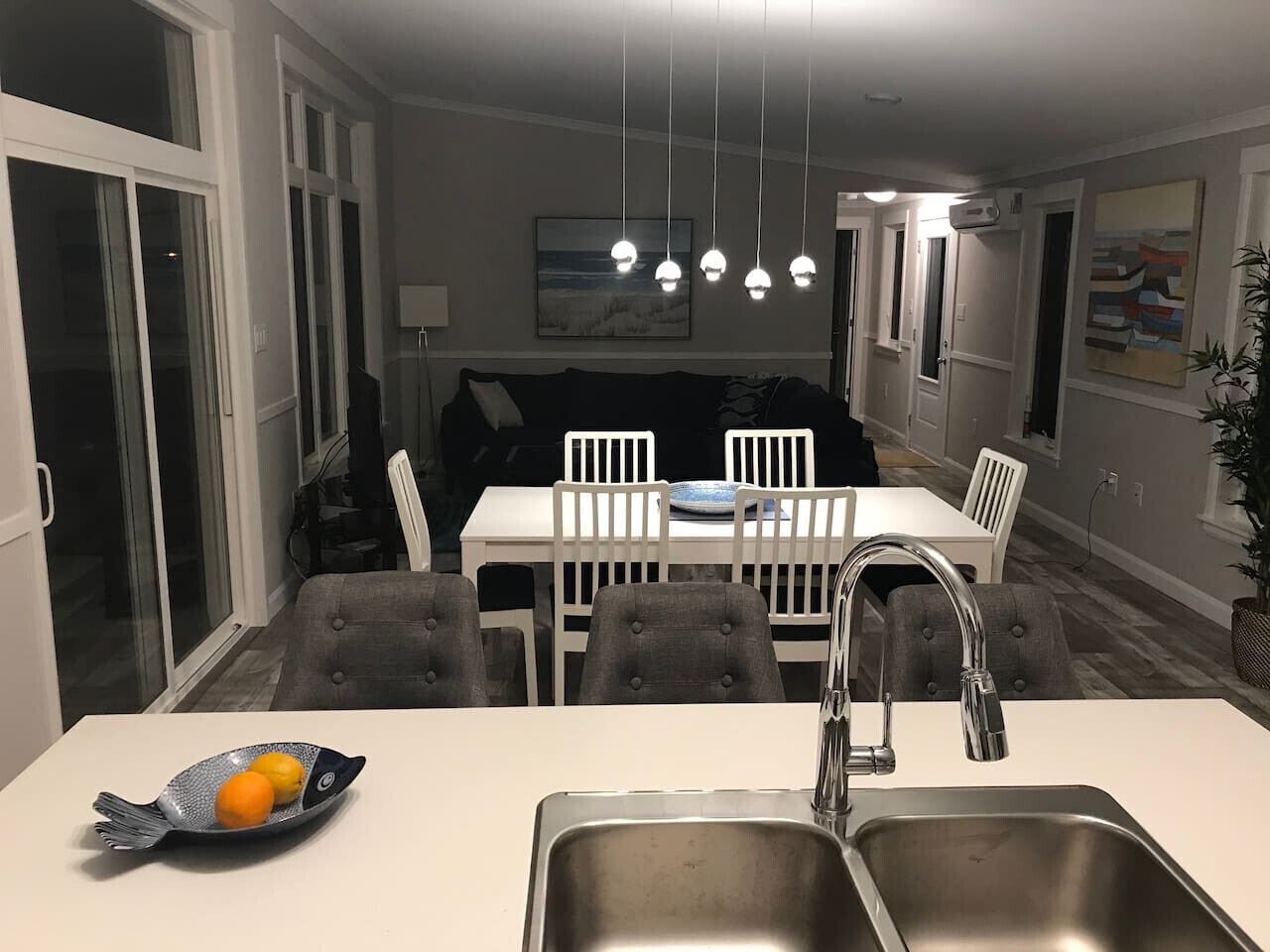 A modern kitchen with a white countertop, stainless steel sink, and a dining area with white chairs and a table.