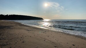 Een strand met een heldere lucht, een kalme zee en een bebost gebied op de achtergrond.