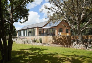 A modern house with large windows, a stone wall, and a grassy yard.