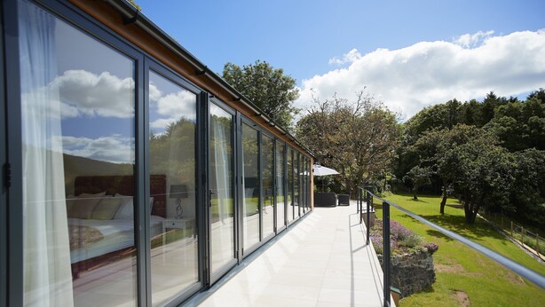 A modern building with large glass windows, a balcony, and a view of a green landscape. - Set in the tranquil Teign Valley, Teign Vale makes the most of its position (Drewsteitgnton)