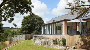 A modern house with large windows, a stone retaining wall, and a well-maintained lawn. - Set in the tranquil Teign Valley, Teign Vale makes the most of its position (Drewsteitgnton)