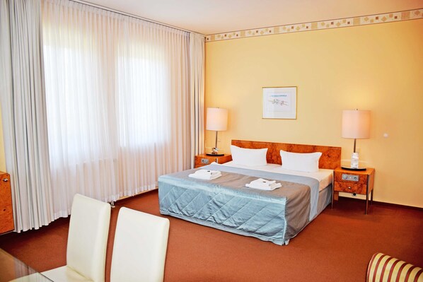 A hotel room with a bed, two bedside tables with lamps, a chair, and a glass table. - 05 Double Room A (H) - The small hotel and apartments on Mönchgut! (Mönchgut)