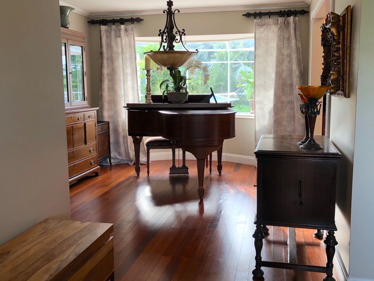 Una habitación con un piano de cola, un aparador de madera y una mesita de noche con una lámpara.