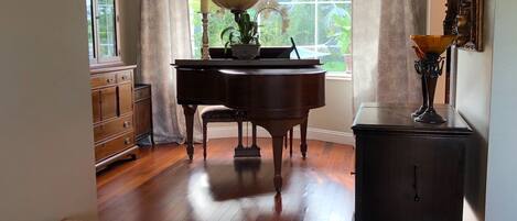 Una habitación con un piano de cola, un aparador de madera y una mesita de noche con una lámpara.