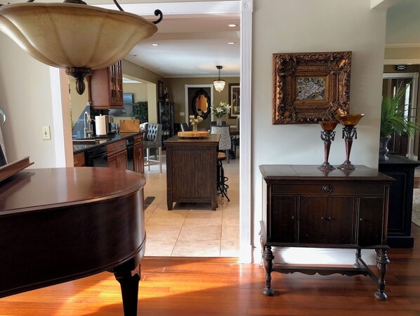 Amplia sala de estar con un piano de cola, una mesa de centro de madera y un mueble de madera oscura con dos objetos parecidos a velas encima.
