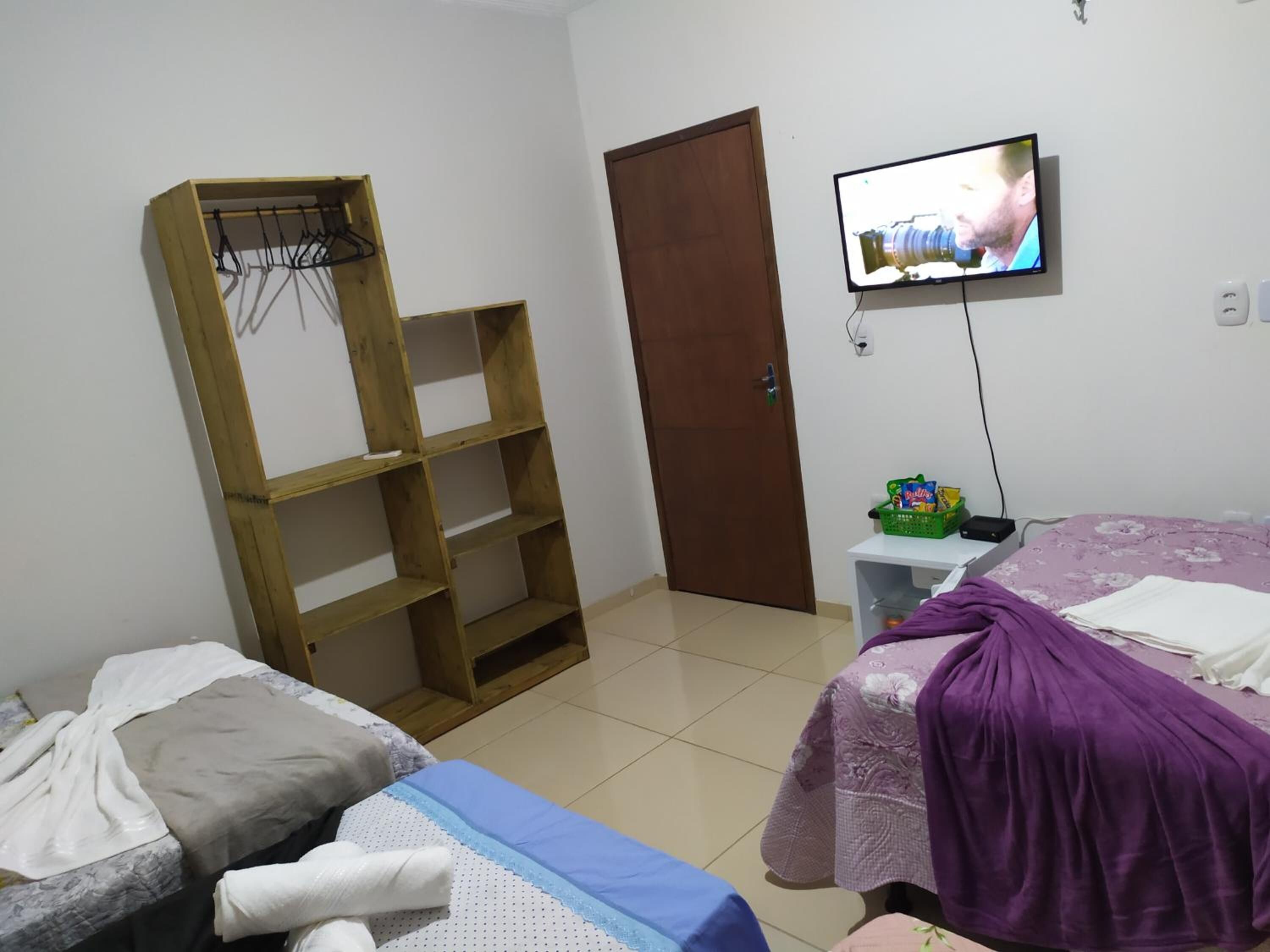 A bedroom with two beds, a wooden shelf unit, a television, and a door.