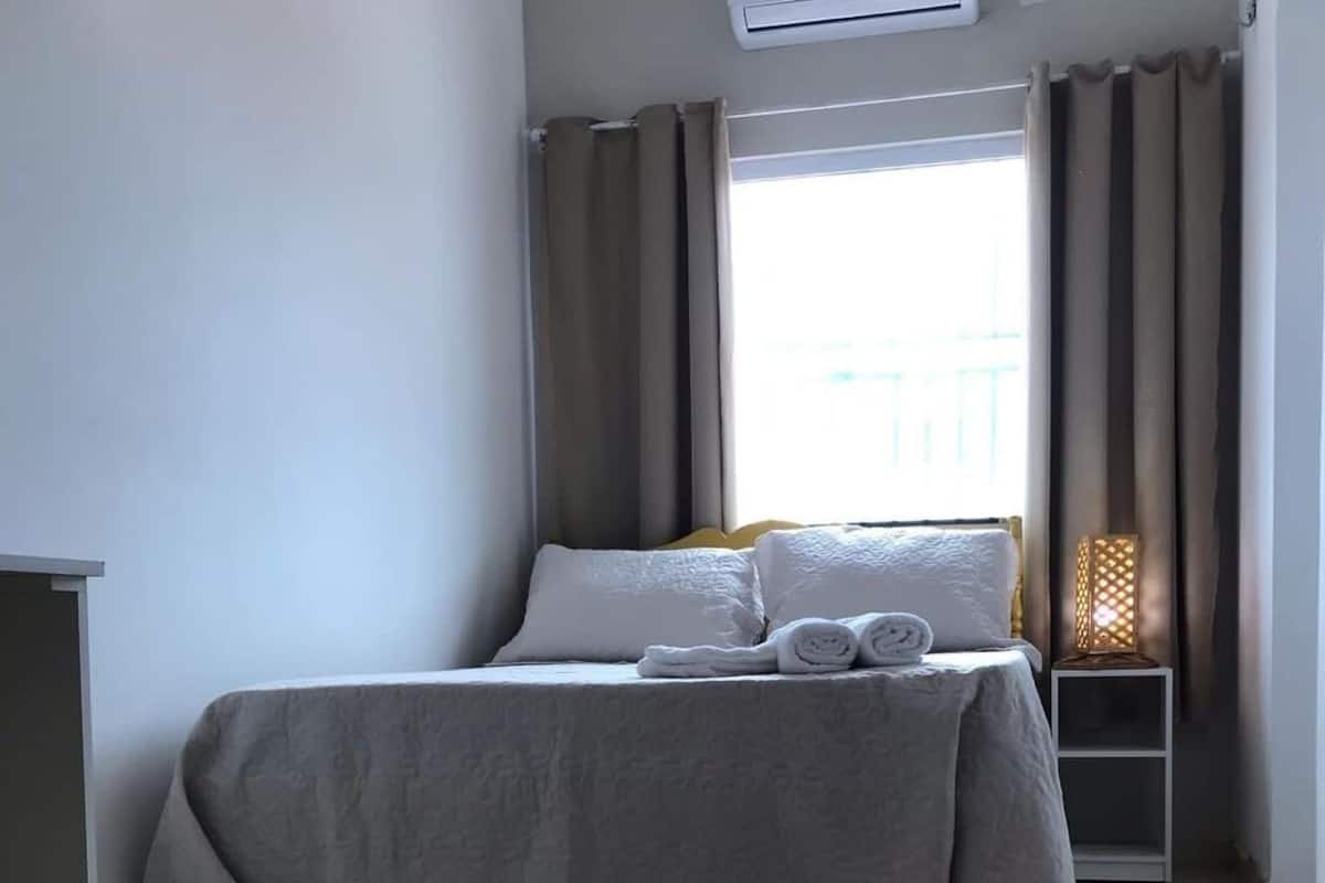 Ein ordentlich eingerichtetes Hotelzimmer mit einem Bett, einem Nachttisch mit Lampe und einem Sessel.