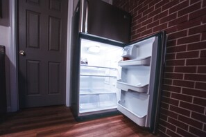 A refrigerator with a freezer compartment, a door, and a brick wall. - A wing in the east of Kingston (Rexburg)