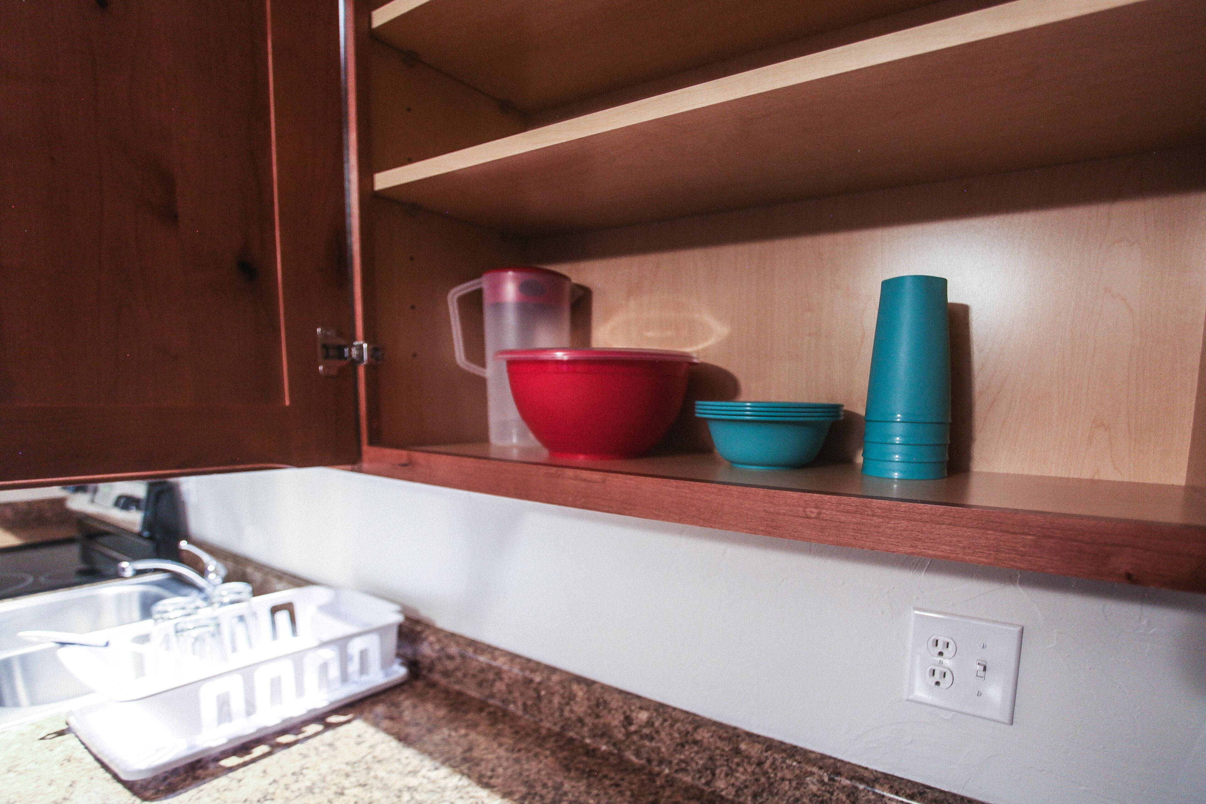 A kitchen with a wooden countertop, a sink, and a shelf with red and blue bowls and a thermos.