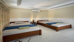 Une chambre d’hôtel avec deux lits en bois, une petite table avec une lampe et un ventilateur de plafond.
