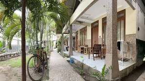 Un espace extérieur abrité, doté d’un chemin en béton, de mobilier en bois et de plantes en pot.