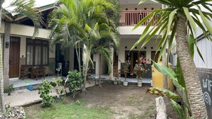Une cour intérieure avec un bâtiment à deux étages, un palmier et des plantes en pot.