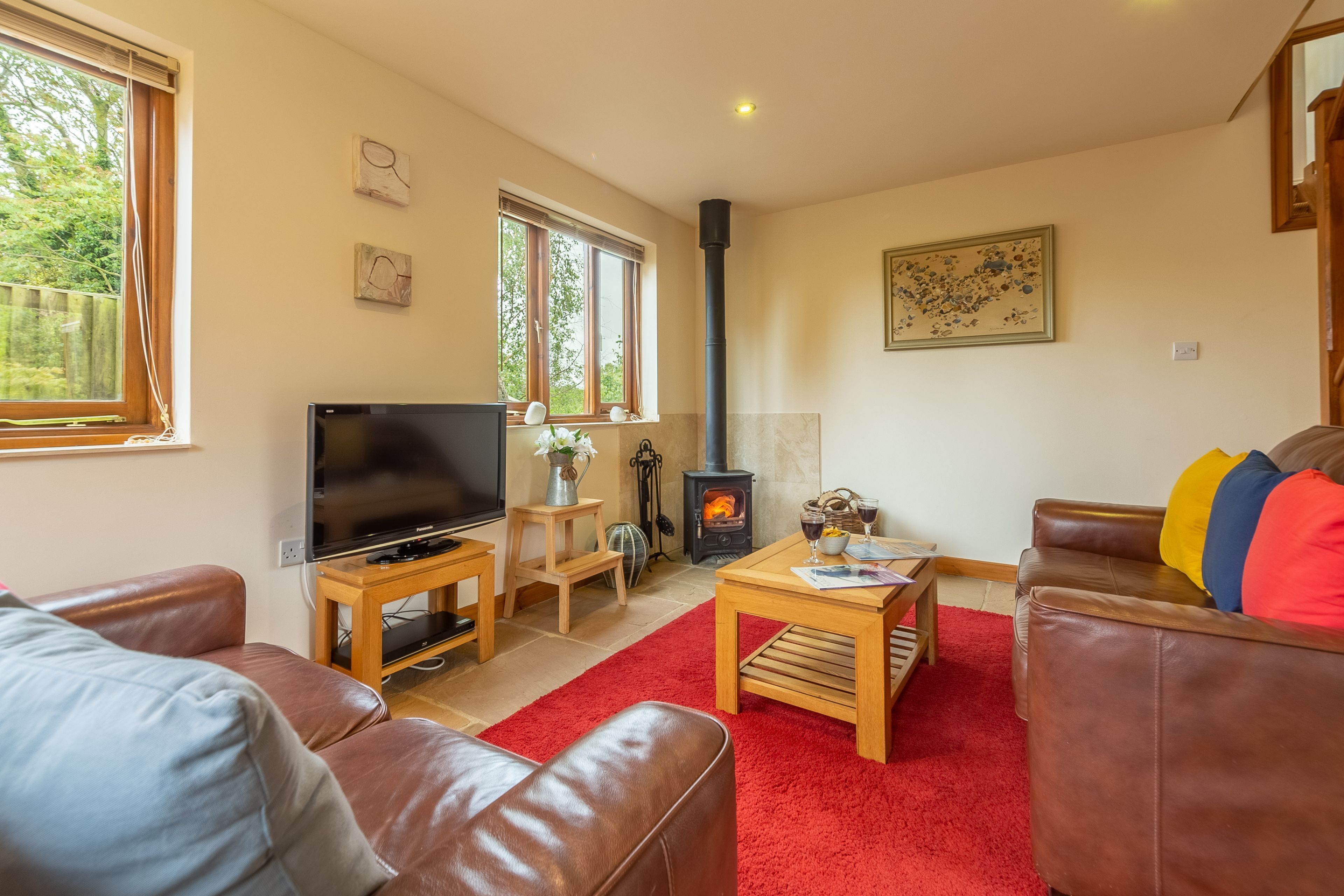 A cozy living room with a fireplace, leather sofas, a TV, and a red rug.