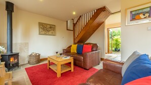 A cozy living room with a fireplace, leather sofas, a red rug, and a wooden coffee table. - Fo'c'sle, Wiveton, Norfolk (Wiveton)