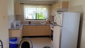 Una cucina compatta con frigorifero, lavello e finestra con tende leggere.
