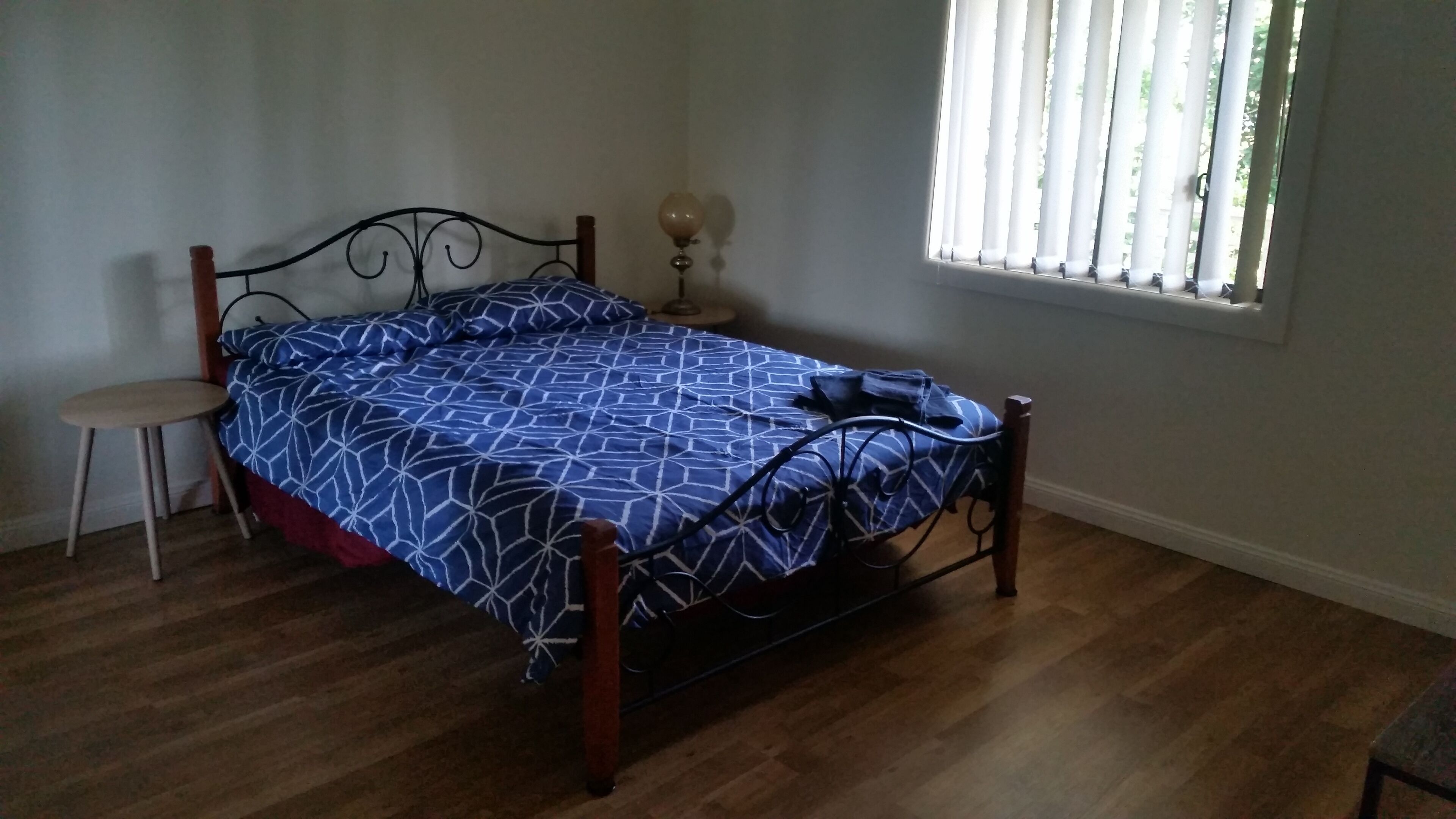 A bedroom with a bed, a nightstand, a lamp, and a window with blinds.