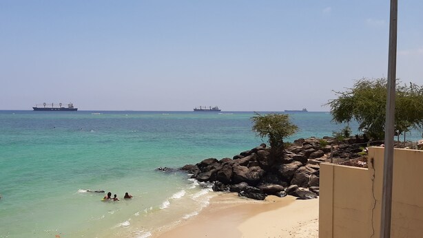 Una platja amb aigua turquesa cristal·lina, un litoral rocosos i vaixells al lluny.
