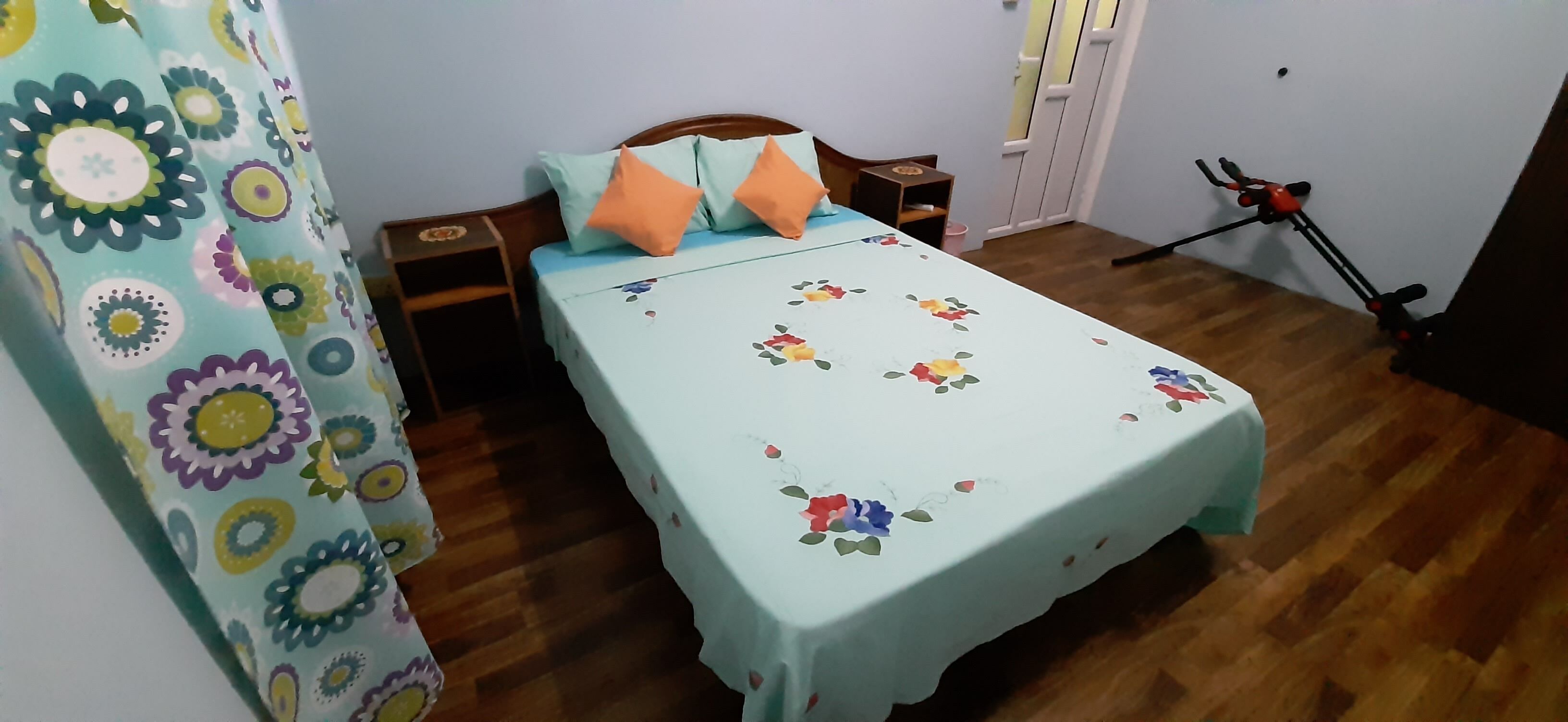 A bedroom with a bed, wooden headboard, two nightstands, a small table, and a bicycle in the corner.