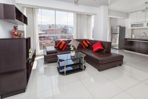 Uma sala de estar moderna com um conjunto de sofá, uma mesa de centro de vidro e vista para a cidade por grandes janelas.