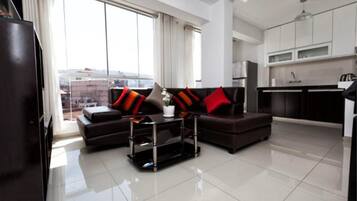 Una sala de estar moderna con un sofá marrón oscuro, una mesa de centro de vidrio y vistas de la ciudad a través de grandes ventanales.