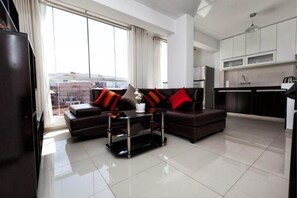 Una sala de estar moderna con un sofá marrón oscuro, una mesa de centro de vidrio y vistas de la ciudad a través de grandes ventanales.