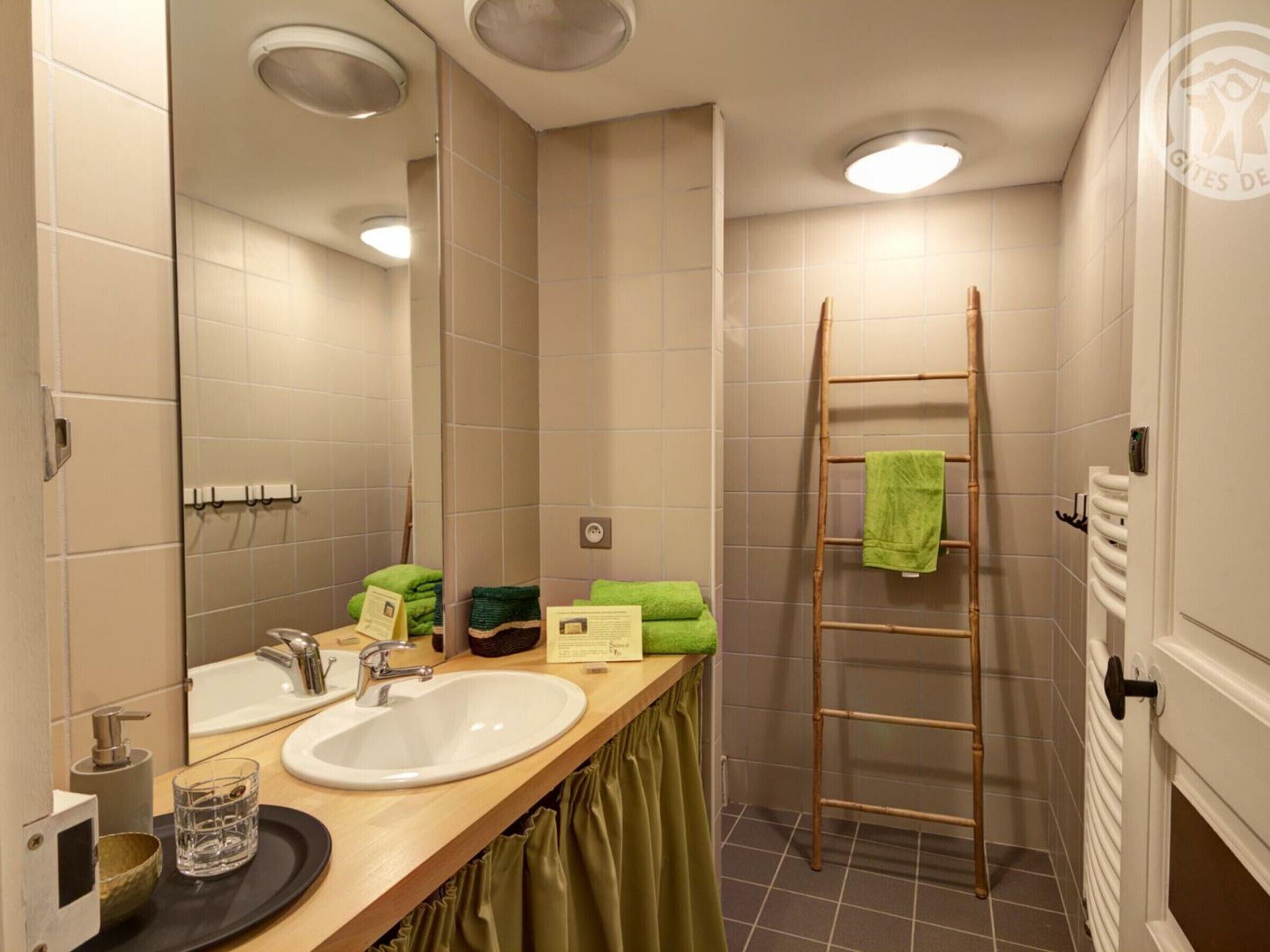 Une salle de bain avec un meuble-lavabo en bois, un évier, un miroir, un porte-serviettes et un espace douche équipé d’une échelle en bois.