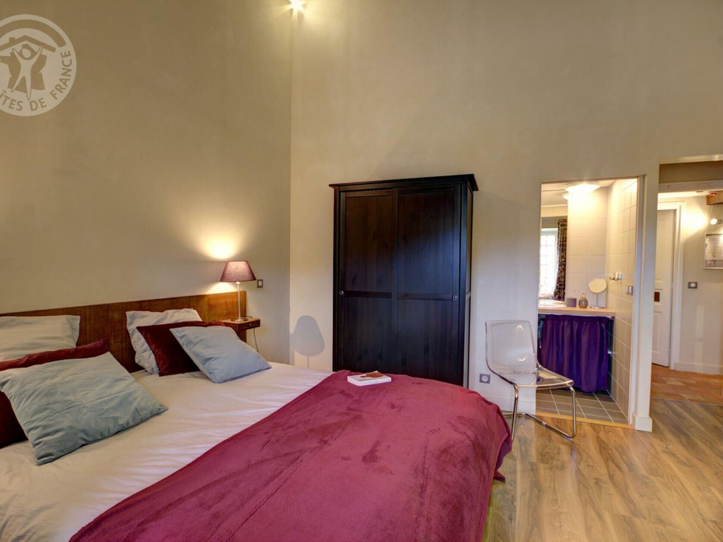 Ein Hotelzimmer mit Bett, Nachttisch, Lampe, Kleiderschrank und einem durchgegangene Tür erkennbaren Badezimmer.